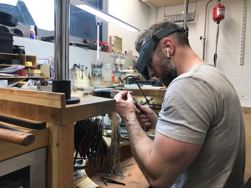 Jeweller working at jewellery bench cuts metal using saw frame 